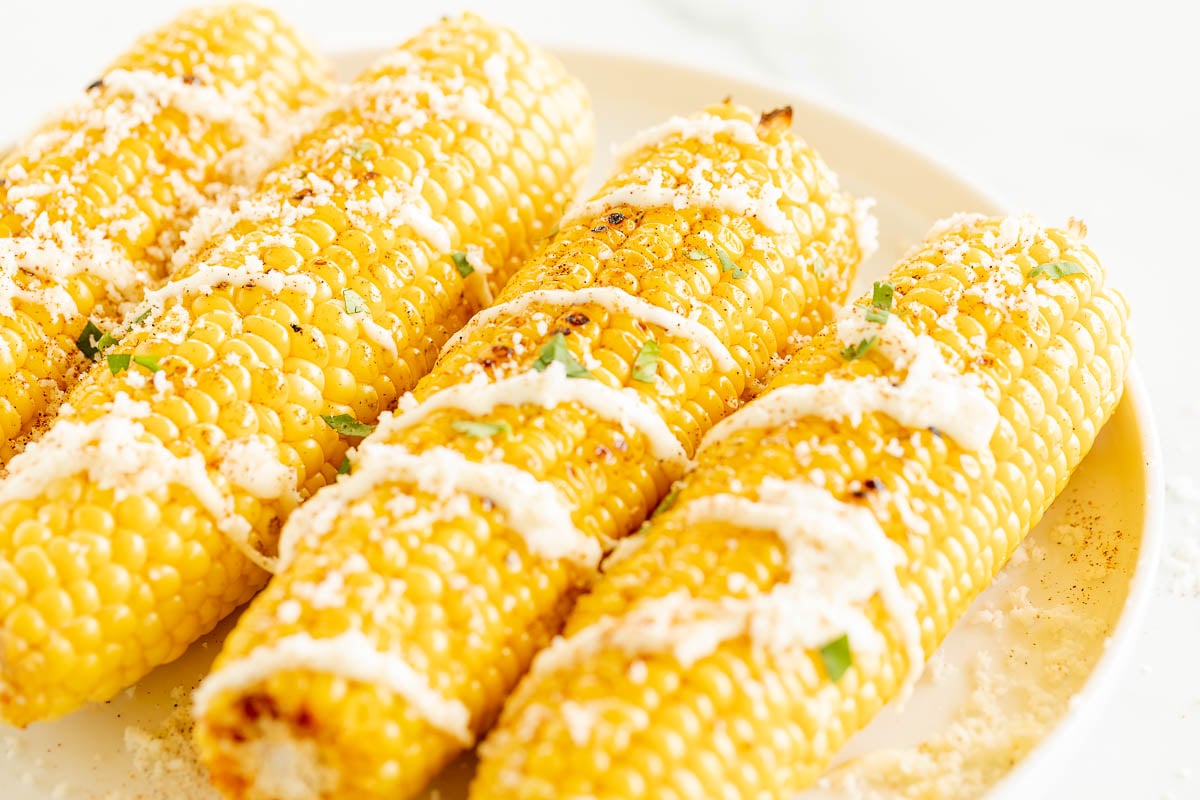 Elote (Mexican corn on the cob) drizzled with crema on a white plate.