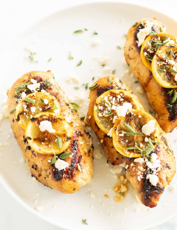 Greek chicken on a white plate, grilled lemon slices on top.