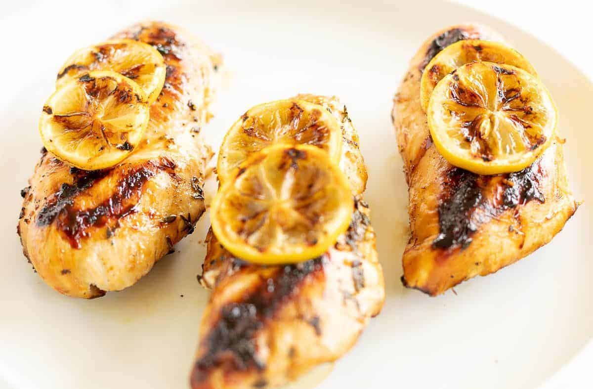 Greek chicken breast on a white plate, topped with grilled lemons and feta cheese and herbs.