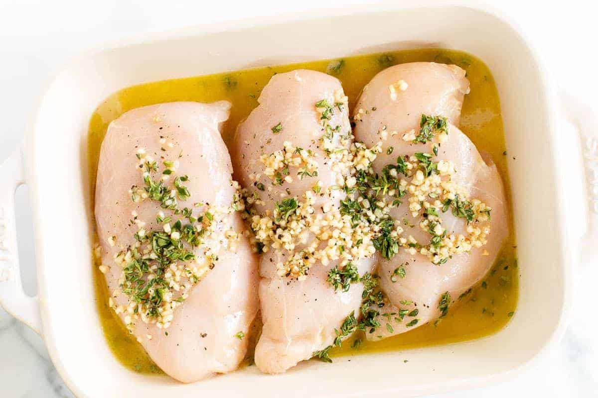 Greek Marinated Chicken breasts in a white baking dish, covered in a greek chicken marinade.
