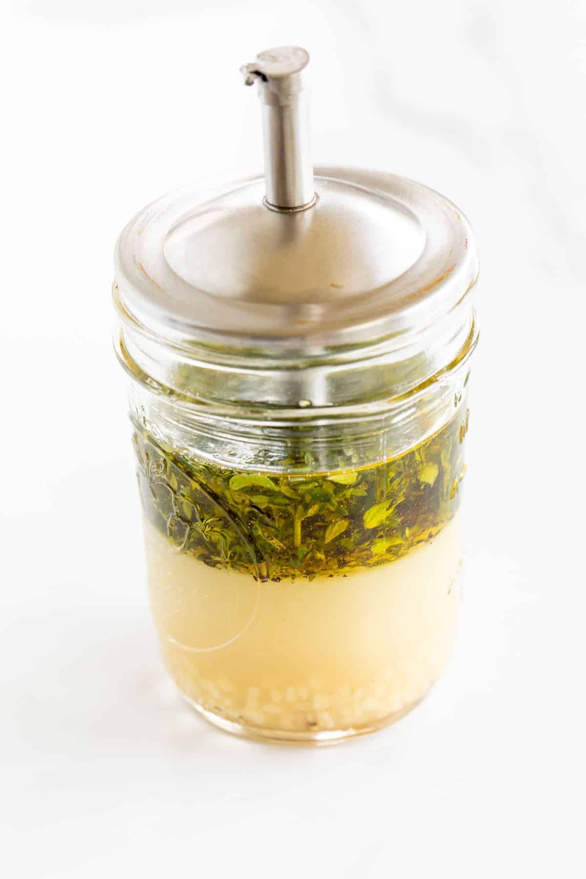 A clear glass mason jar full of Greek chicken marinade.