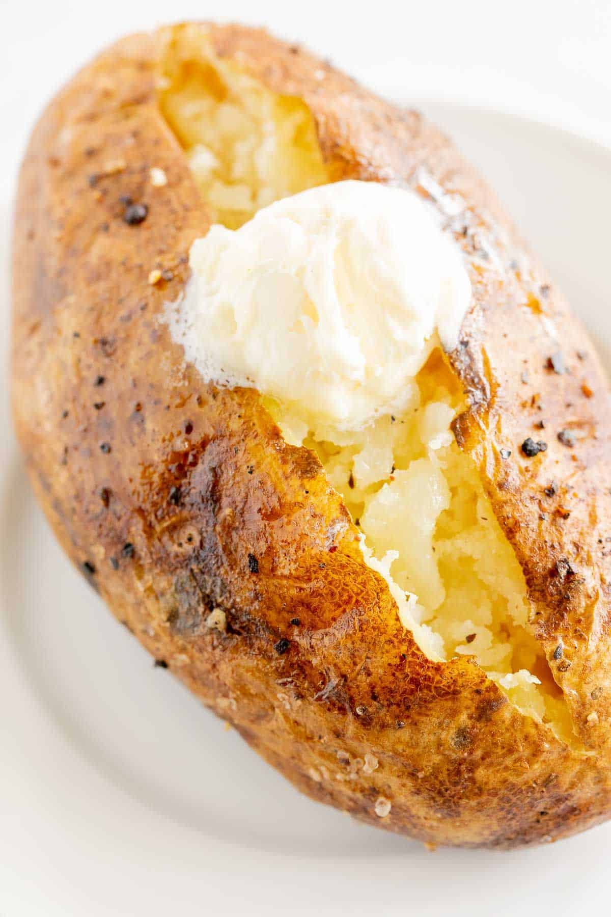 A single grilled baked potato on a white plate, topped with butter and sour cream.