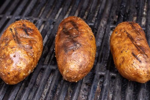 Grilled baked potatoes on a grill grate.