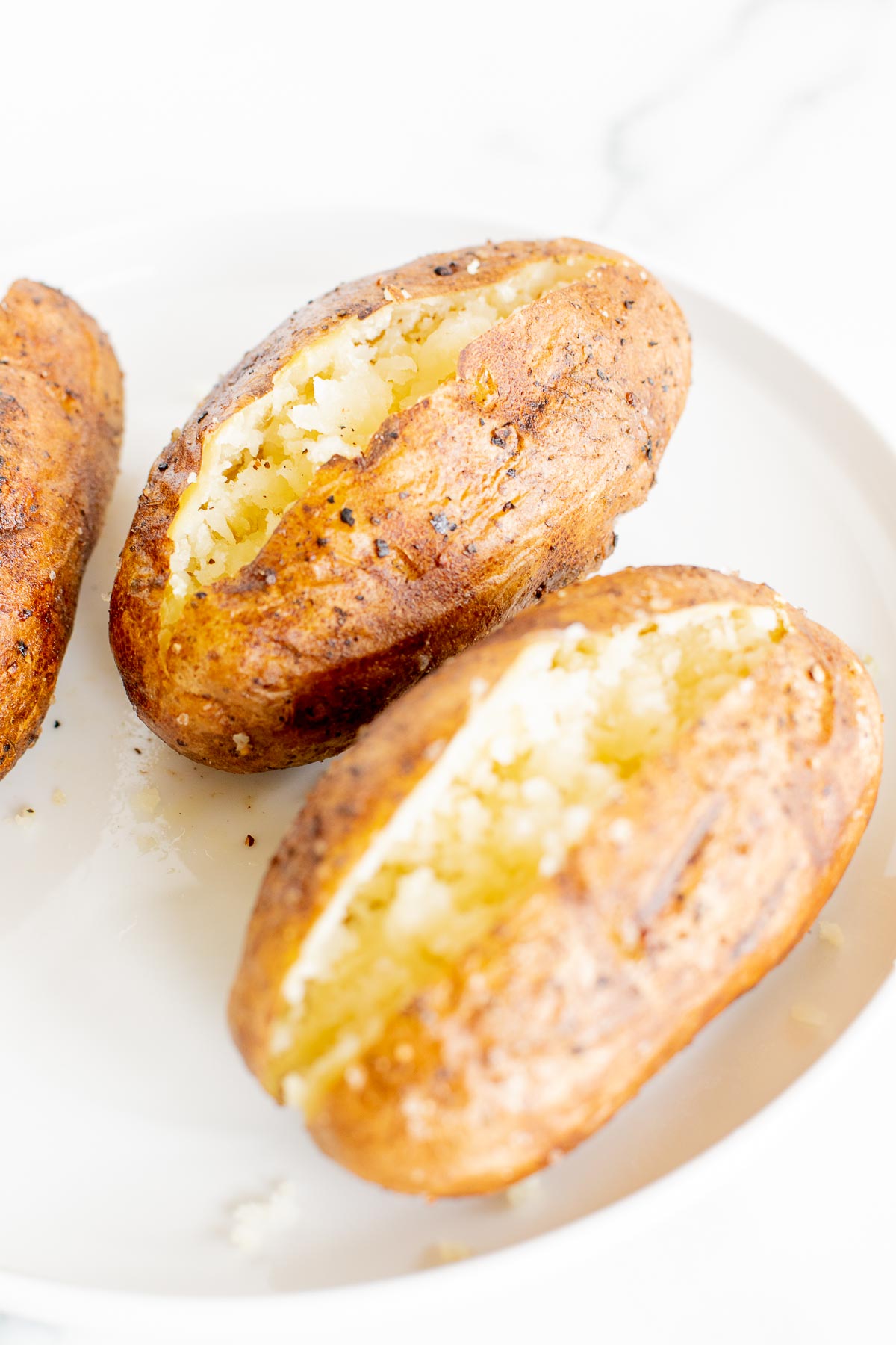 grilled baked potatoes sliced open and placed on a white plate.