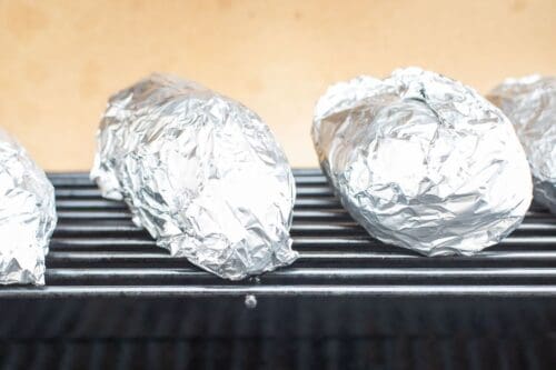 Grilled baked potatoes in foil on a grill grate.
