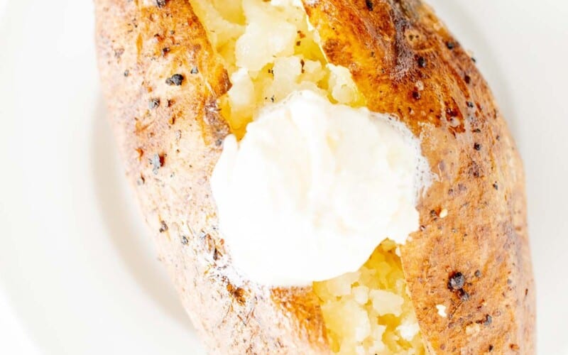 A single BBQ baked potato on a white plate, topped with butter and sour cream.