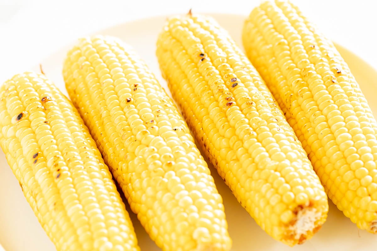 Grilled sweet corn on the cobs on a white plate with some char marks visible.