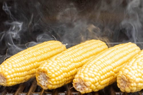 Grilled Sweet Corn on the cob grilling on a barbecue, with steam rising from the hot surface.