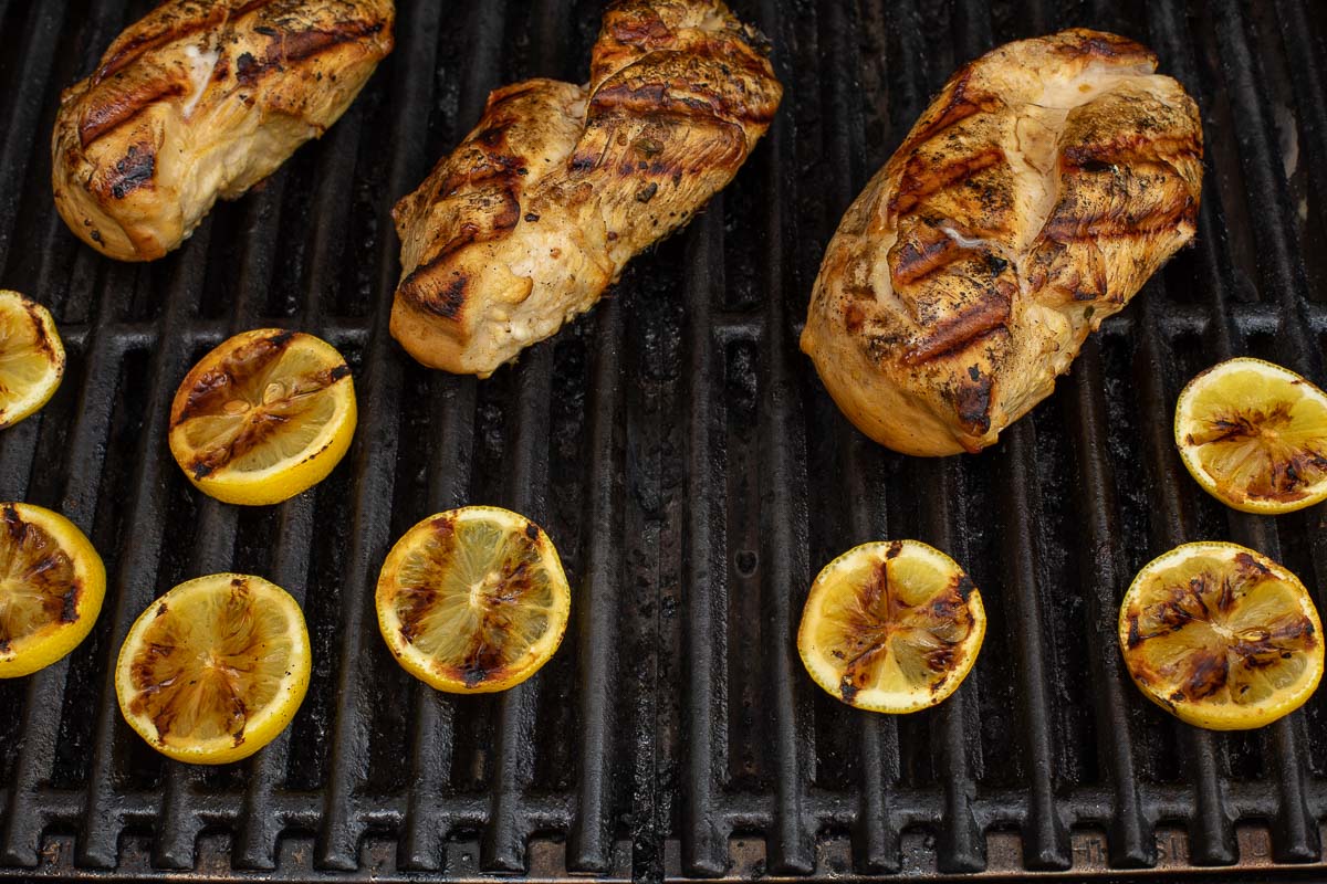 Grilled Greek chicken and lemon slices on a gas grill.