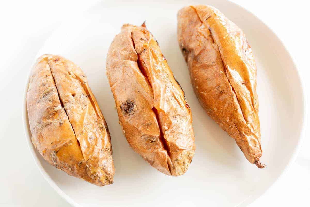 Grilled sweet potatoes on a white plate, cut open down the center.