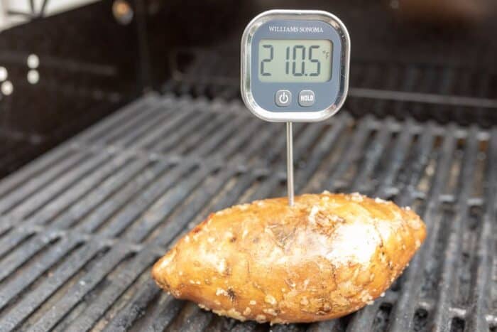 A sweet potato on a grill with a digital thermometer stuck in it.