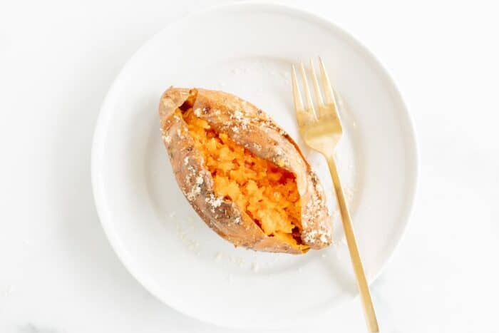 A grilled sweet potato on a white plate, gold fork to the side.