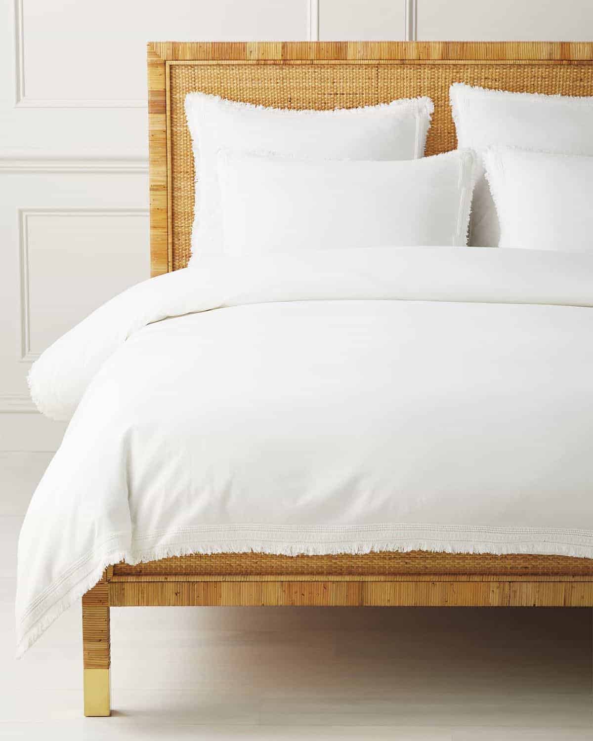 A rattan bed frame with white bedding and layered pillows from Serena and Lily.