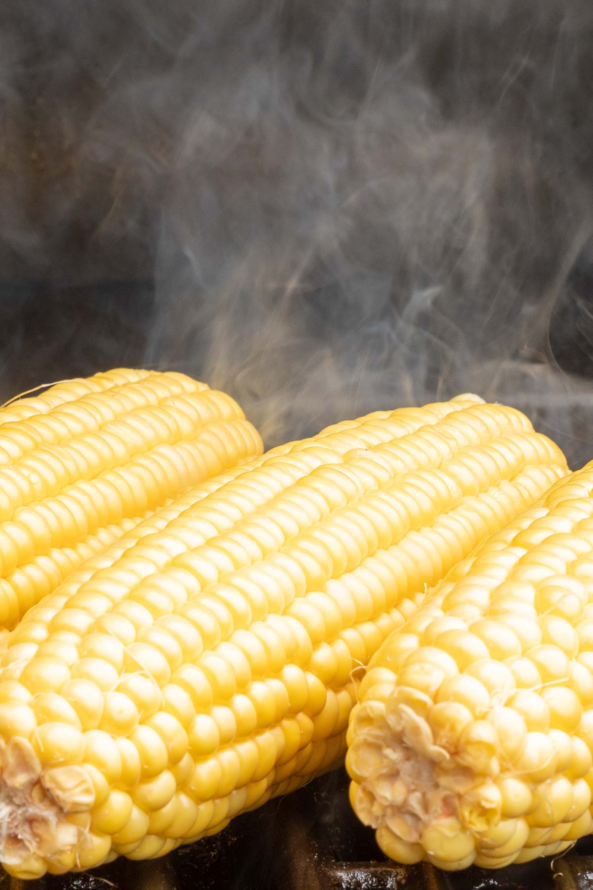Three ears of grilled corn on the cob with steam rising in the background.