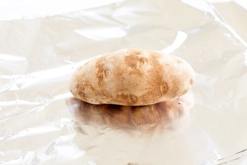 A single russet potato laid on a sheet of aluminum foil.