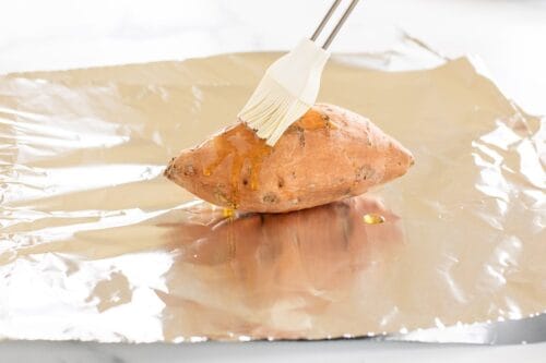A sweet potato resting on a piece of aluminum foil.