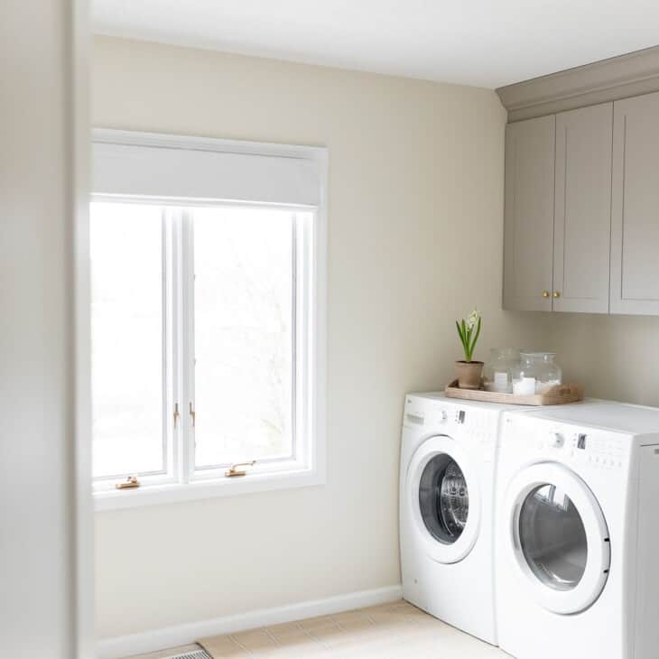 A laundry room with white washer and dryer, gold light fixture and white walls and white baseboards
