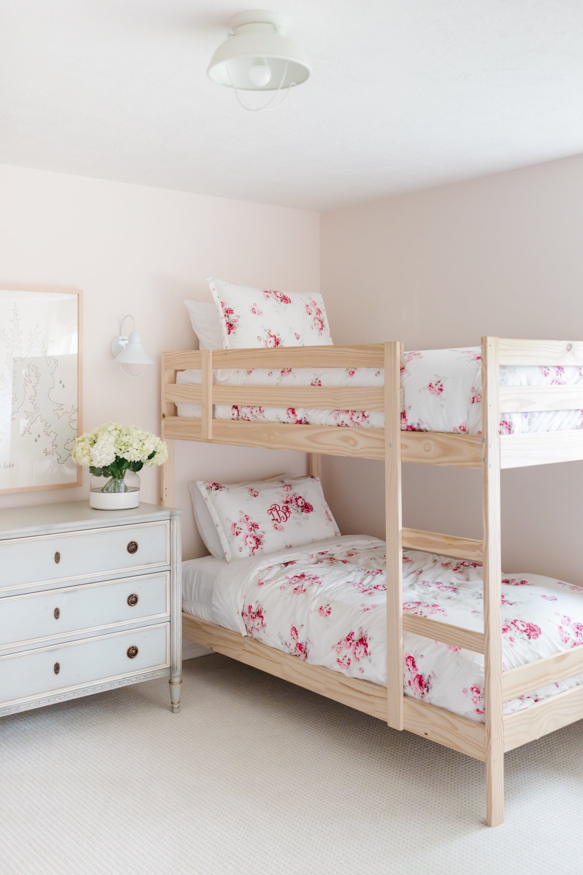 A pale pink girl's bedroom with wooden bunk beds and wall to wall carpet