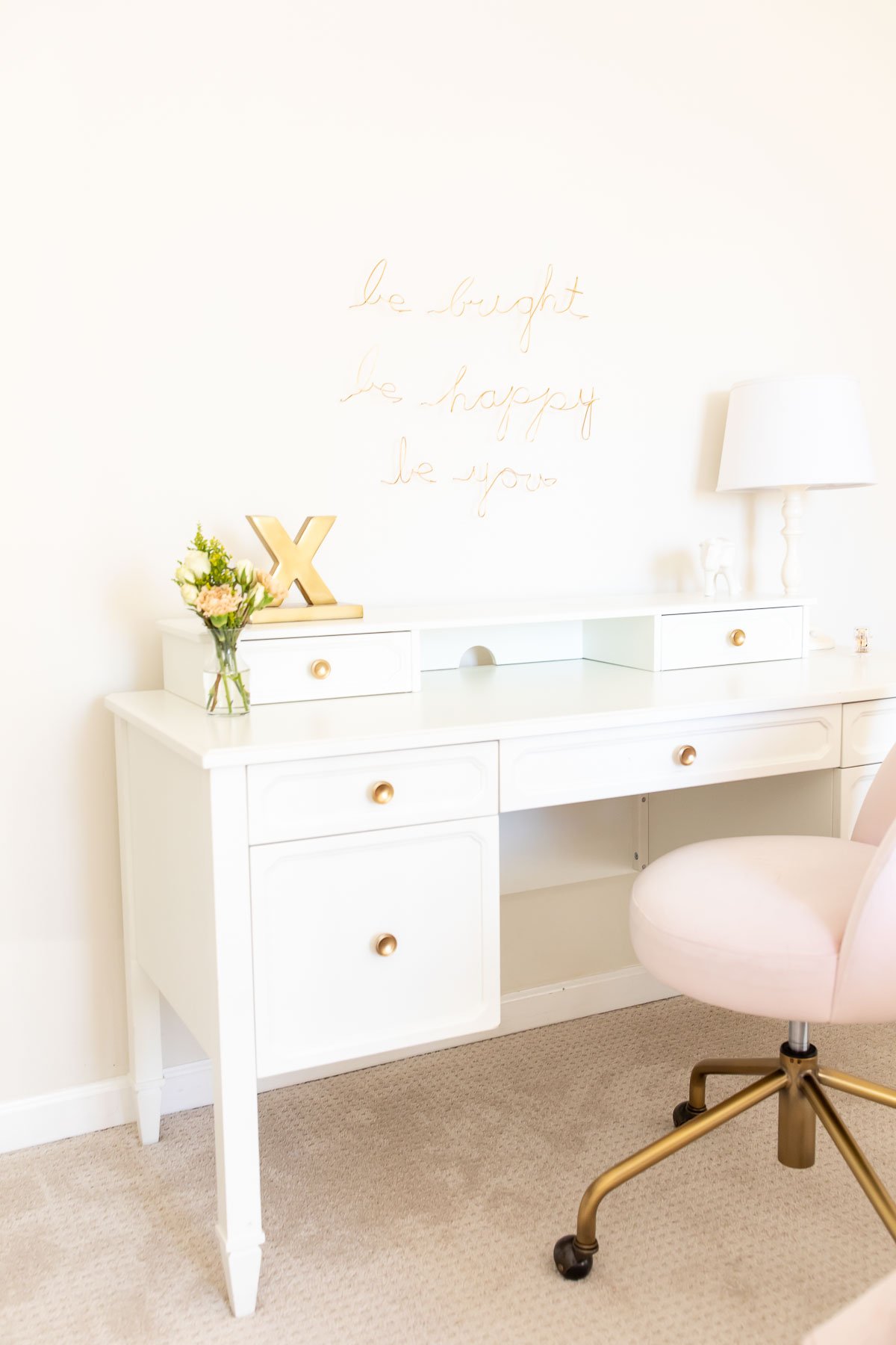 A white bedroom with a desk and wire art work above it.