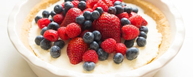 lemon pie topped with berries in white pie dish