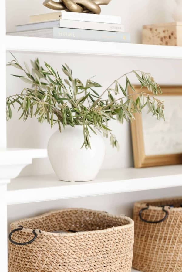 Bookshelf decor ideas of baskets, white pottery and artwork on white built ins.