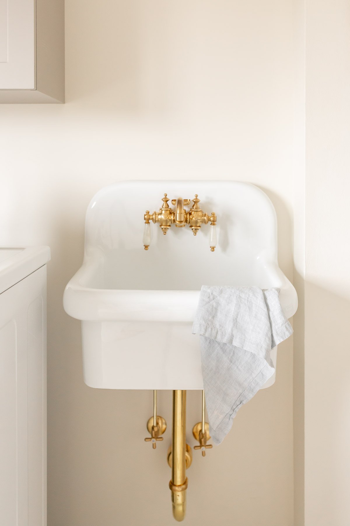 A white wall mount sink with brass hardware.