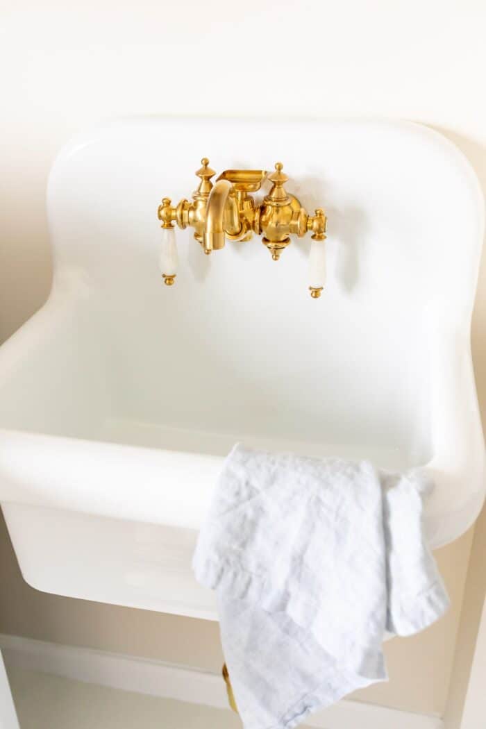 A white wall mount sink with brass hardware.
