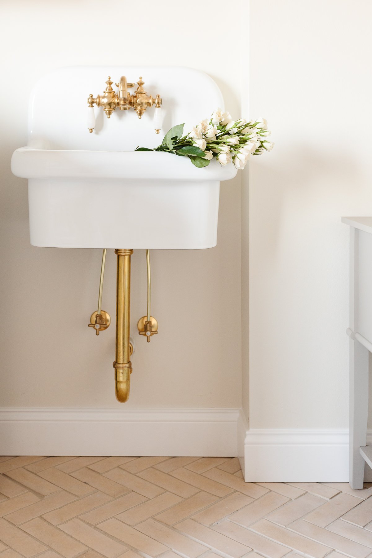 A white wall mount sink with brass hardware.