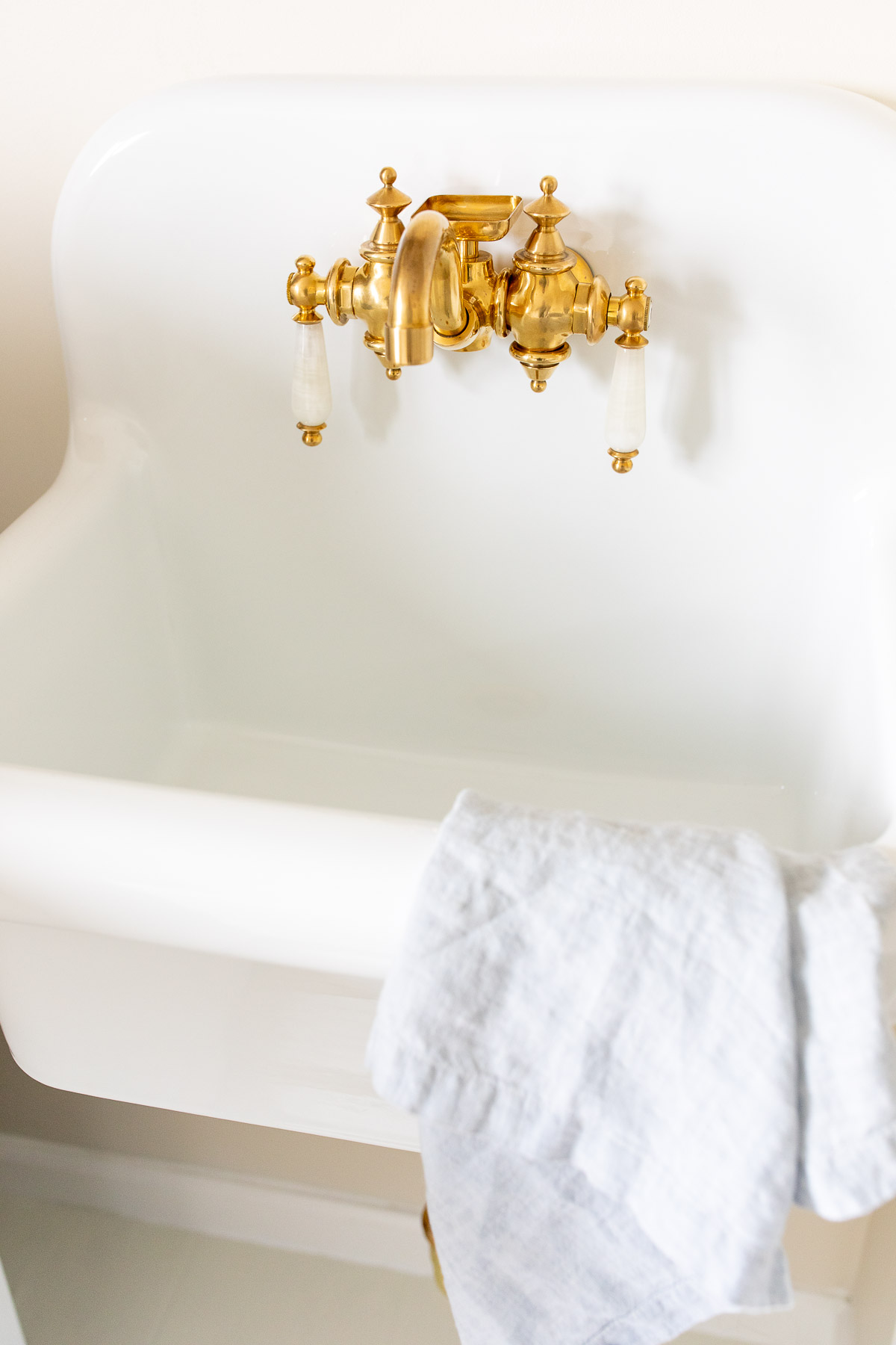 A white ceramic wall mounted sink with brass hardware.