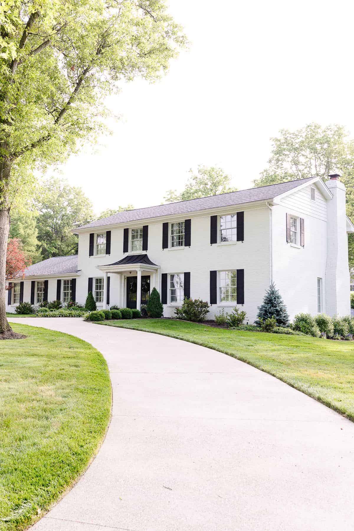 A colonial white brick house with a curved driveway.
