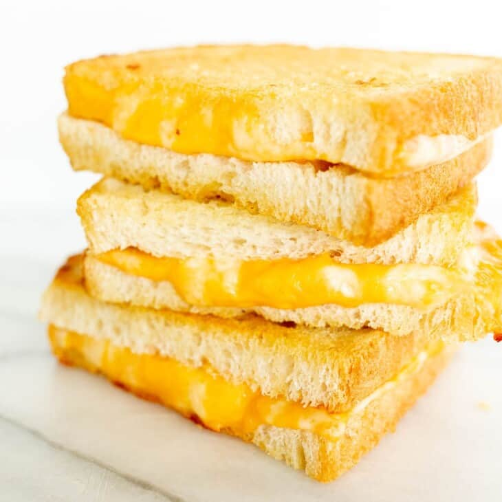 A stack of oven grilled cheese sandwiches, sliced on a white surface.