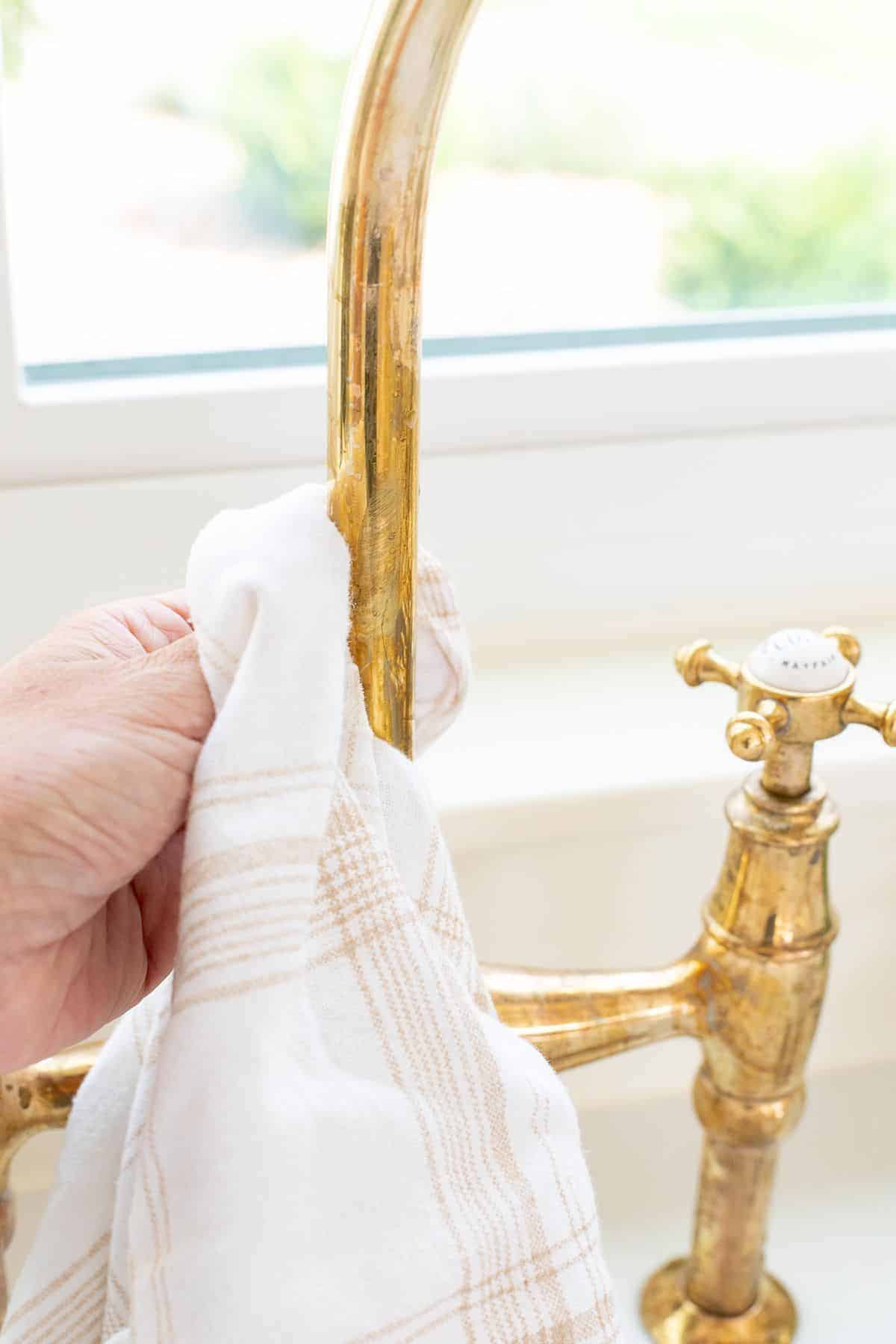 A tarnished brass faucet being scrubbed with a soft cloth.