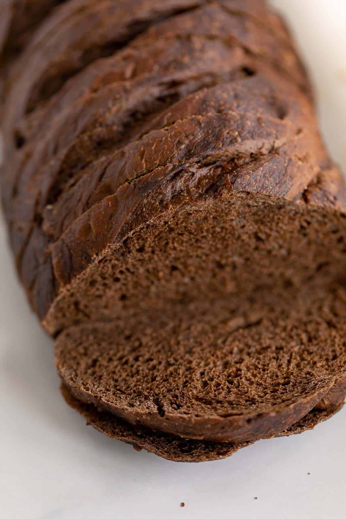 A loaf of dark rye bread, sliced on a marble countertop.