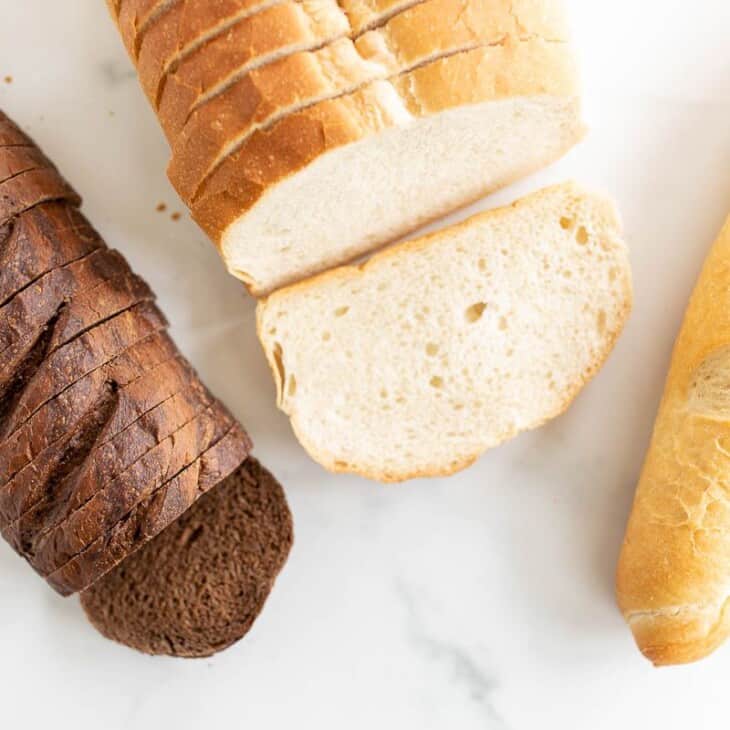 Three different loaves of bread on a marble surface, in a post about the best bread for grilled cheese.