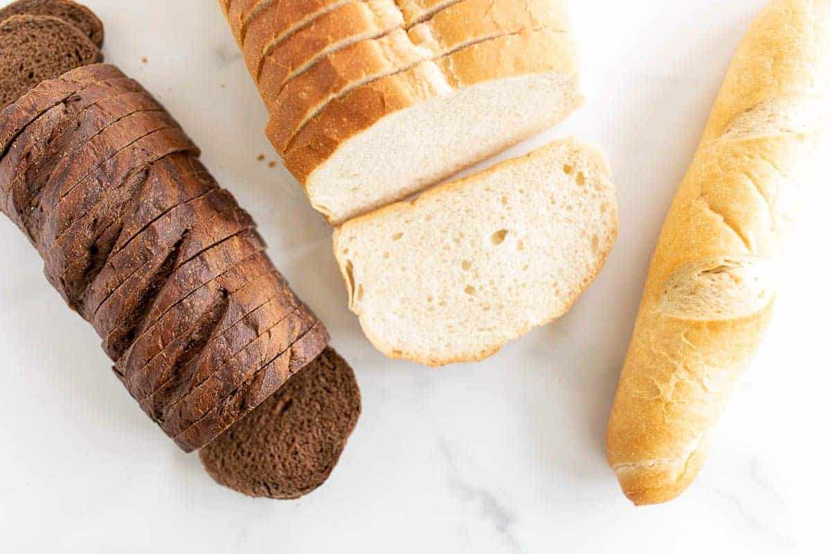 Three different loaves of bread on a marble surface, in a post about the best bread for grilled cheese.