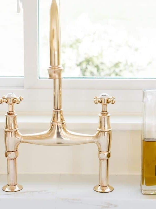A brass bridge faucet that is shiny from brass polish, bottle of olive oil to the side.