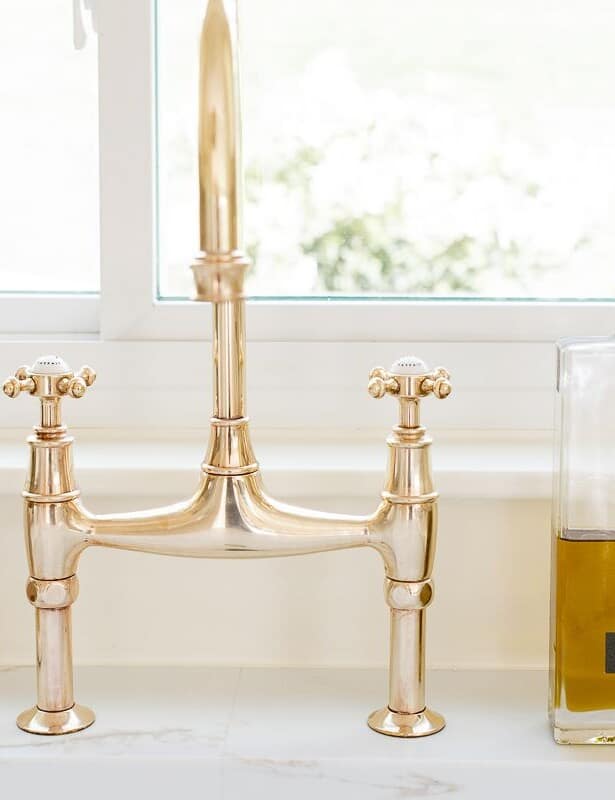 A brass bridge faucet that is shiny from brass polish, bottle of olive oil to the side.