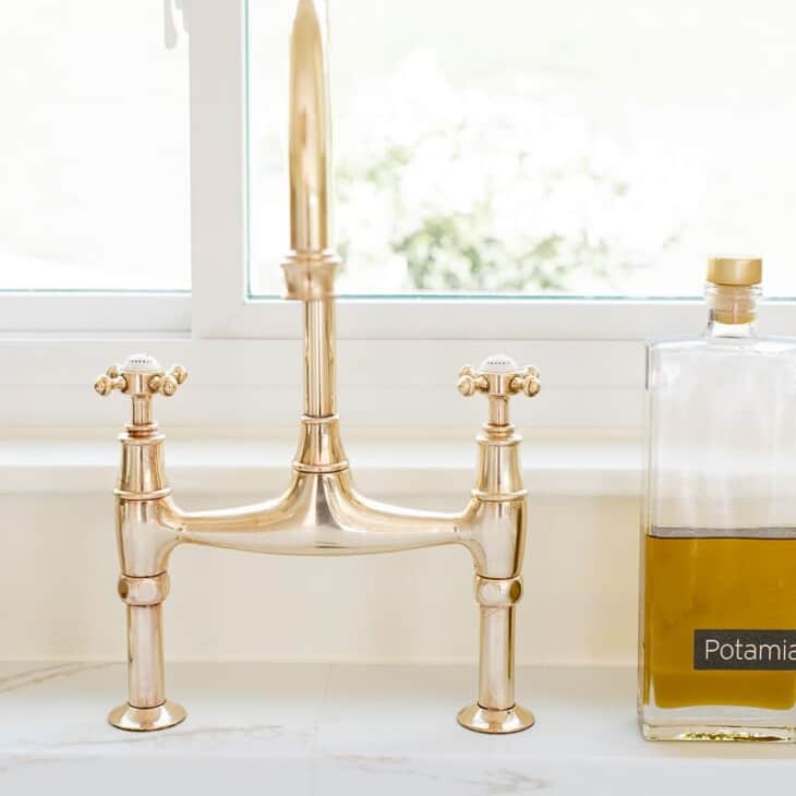 A brass bridge faucet that is shiny from brass polish, bottle of olive oil to the side.
