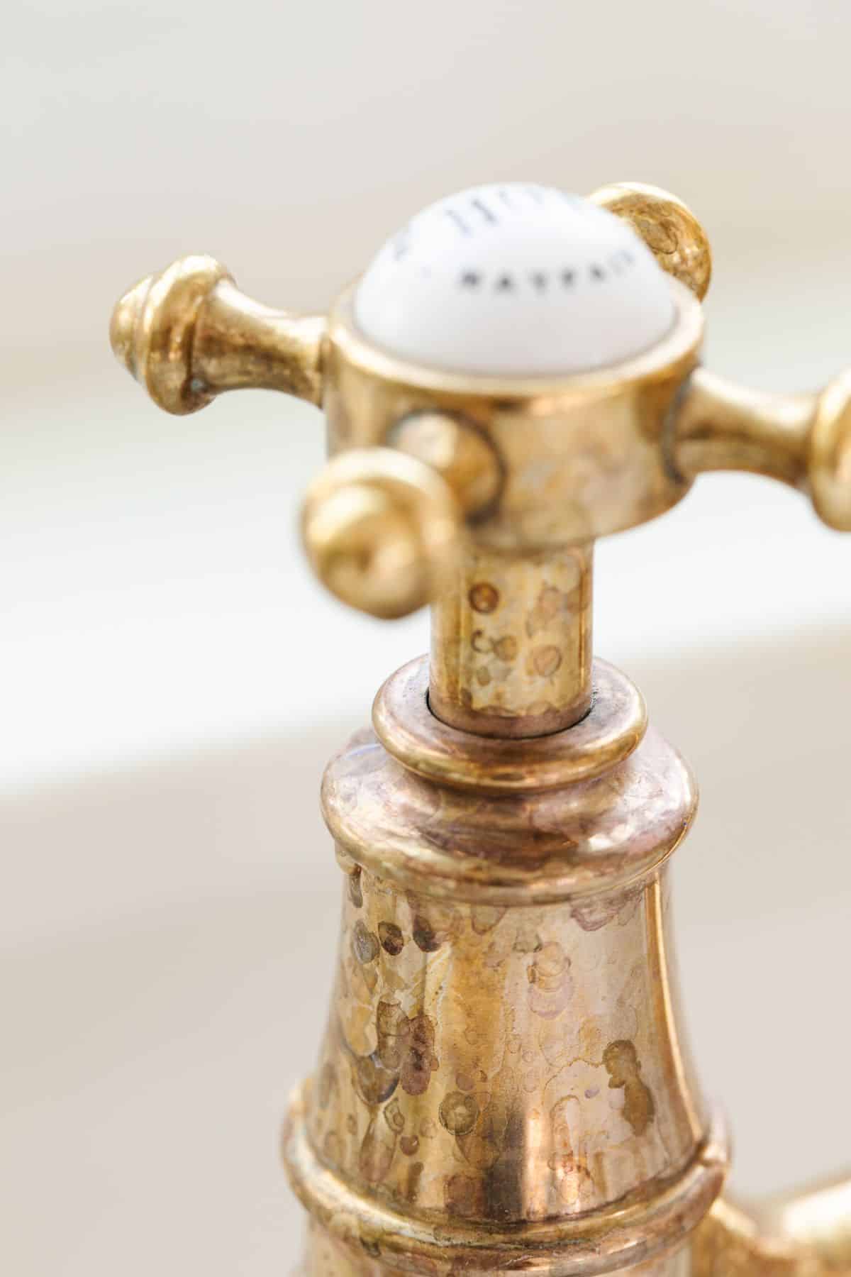 A brass kitchen faucet with some tarnish at the handle.