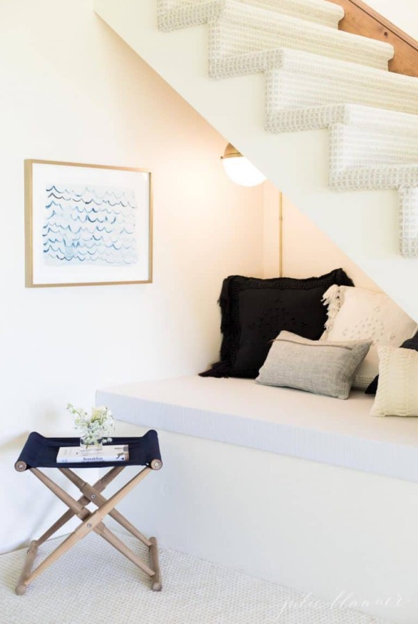 A nook under the stairs of a home with pillows, a wall sconce and art.