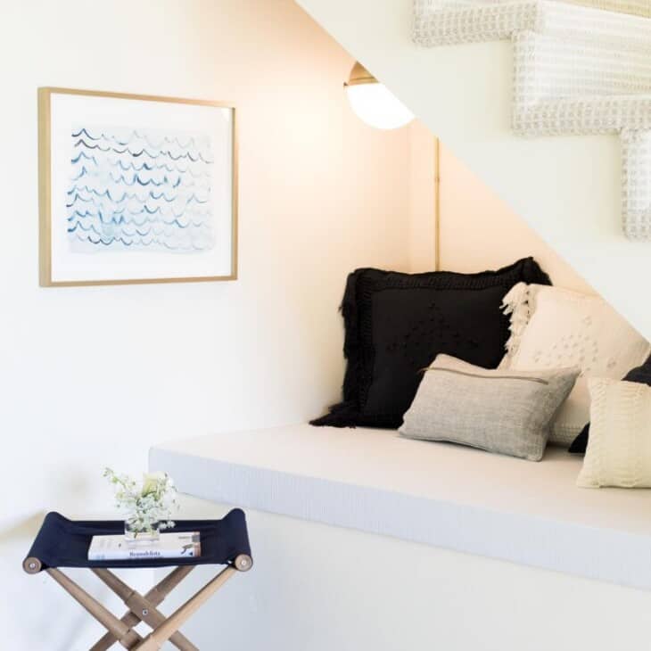 A nook under the stairs of a home with pillows, a wall sconce and art.