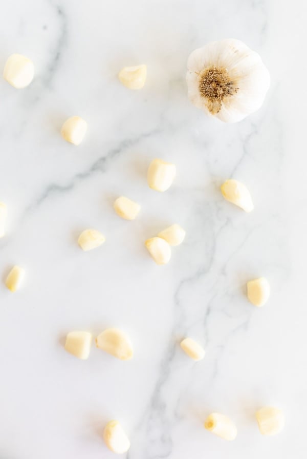 A single head of garlic and more garlic cloves open onto a marble countertop.
