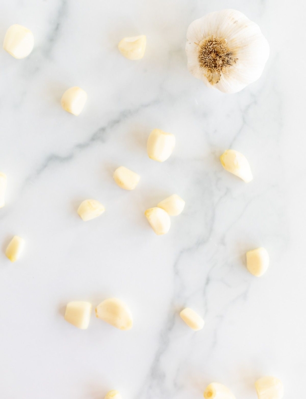 A single head of garlic and more garlic cloves open onto a marble countertop.
