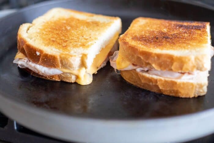 Two grilled ham and cheese sandwiches on a black cast iron pan.