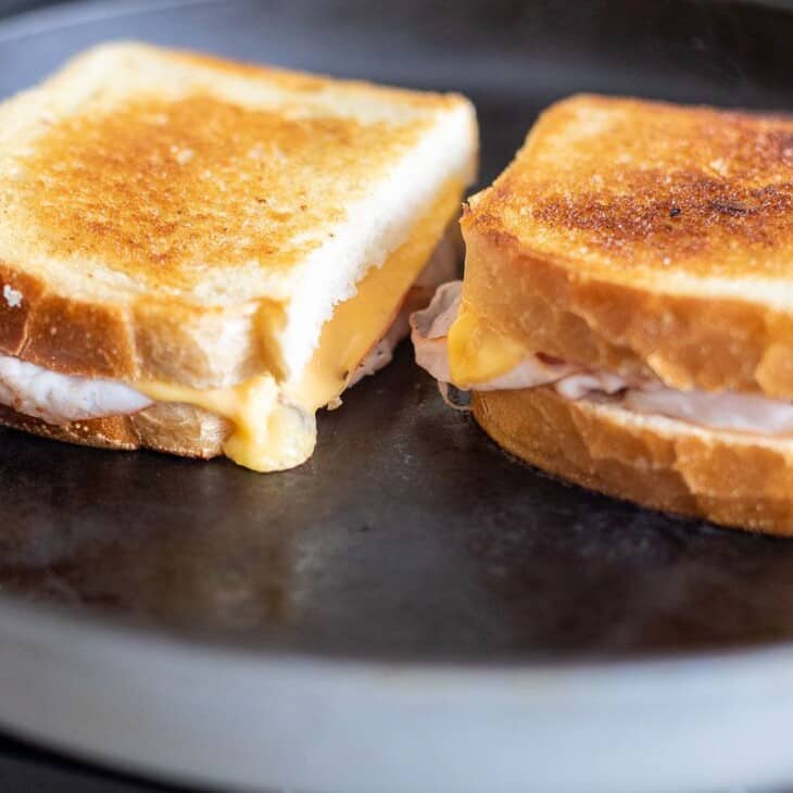 Two grilled ham and cheese sandwiches on a black cast iron pan.