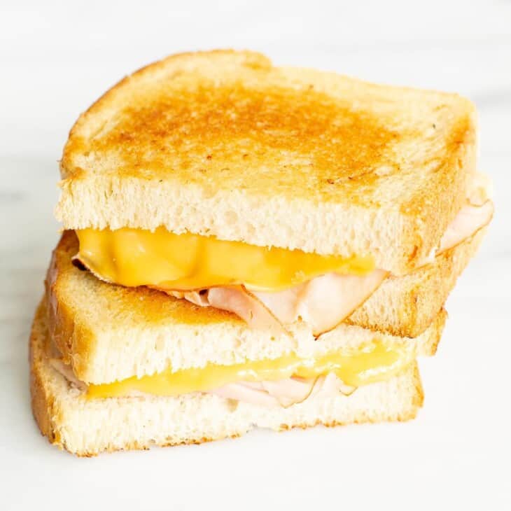 sliced grilled ham and cheese on white bread on a marble surface.