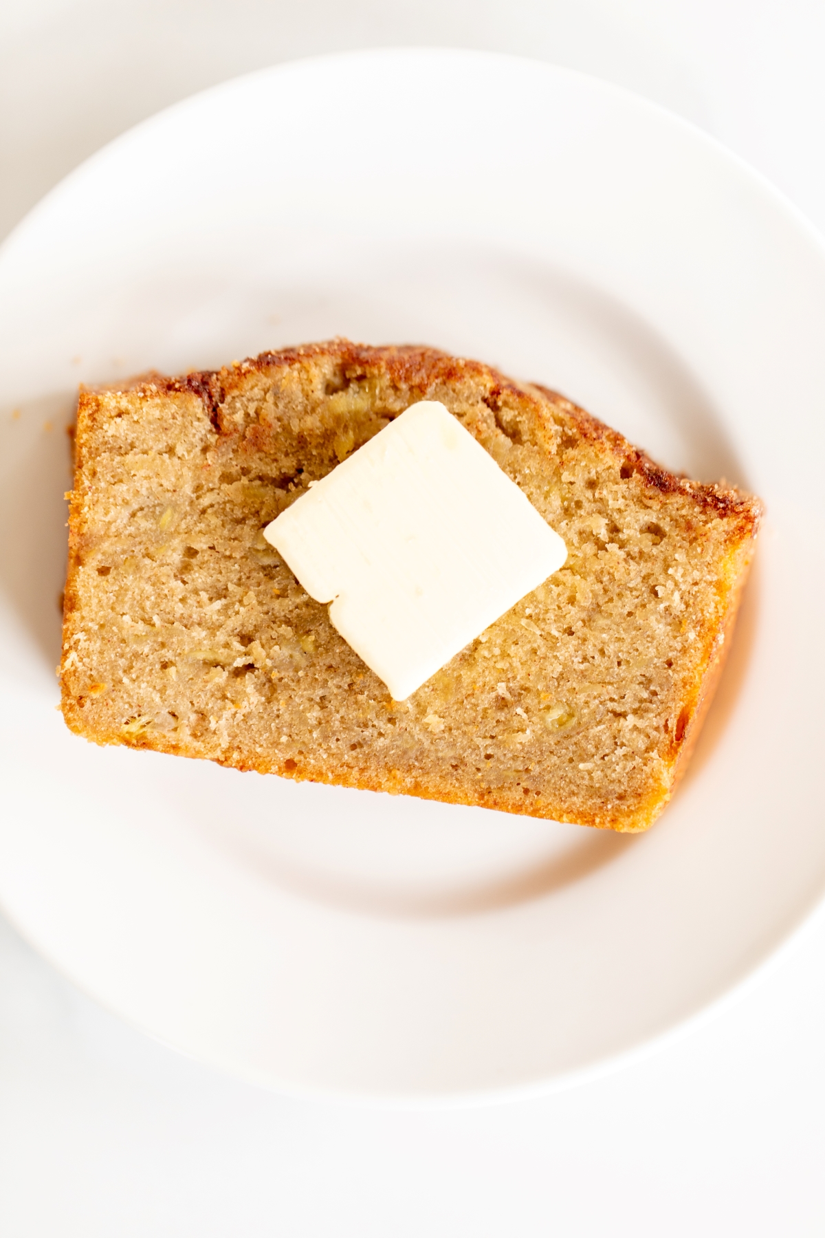A slice of banana bread on a white plate, with a pat of butter