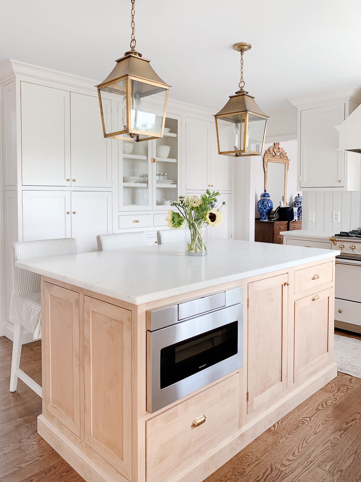 A light oak wood kitchen island with a built in microwave, surrounding cabinets are cream.