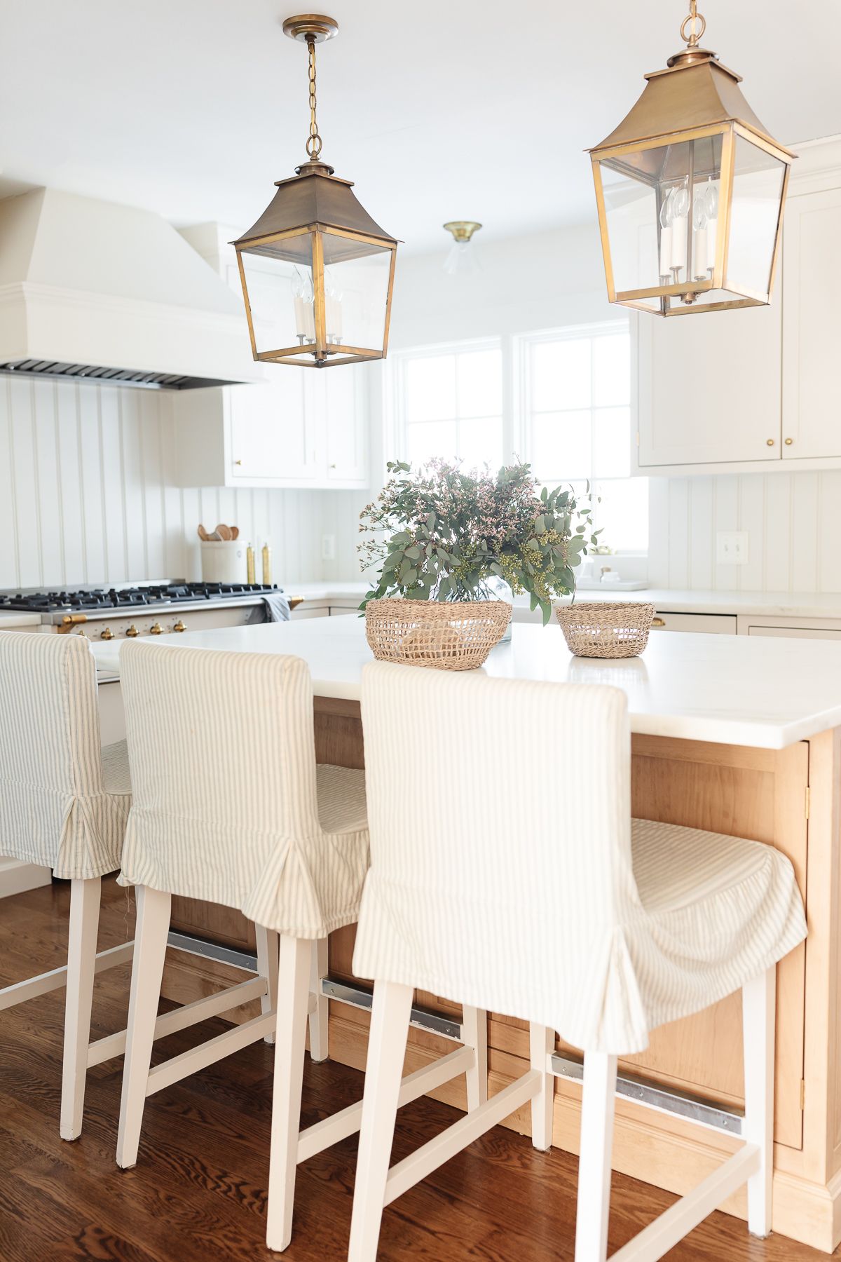 A light oak wood kitchen island with striped fabric bar stools, surrounding cabinets are cream. 