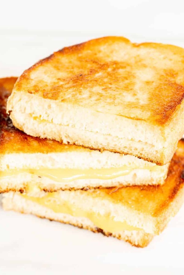 A stack of sliced grilled cheese with mayonnaise on a white marble surface.